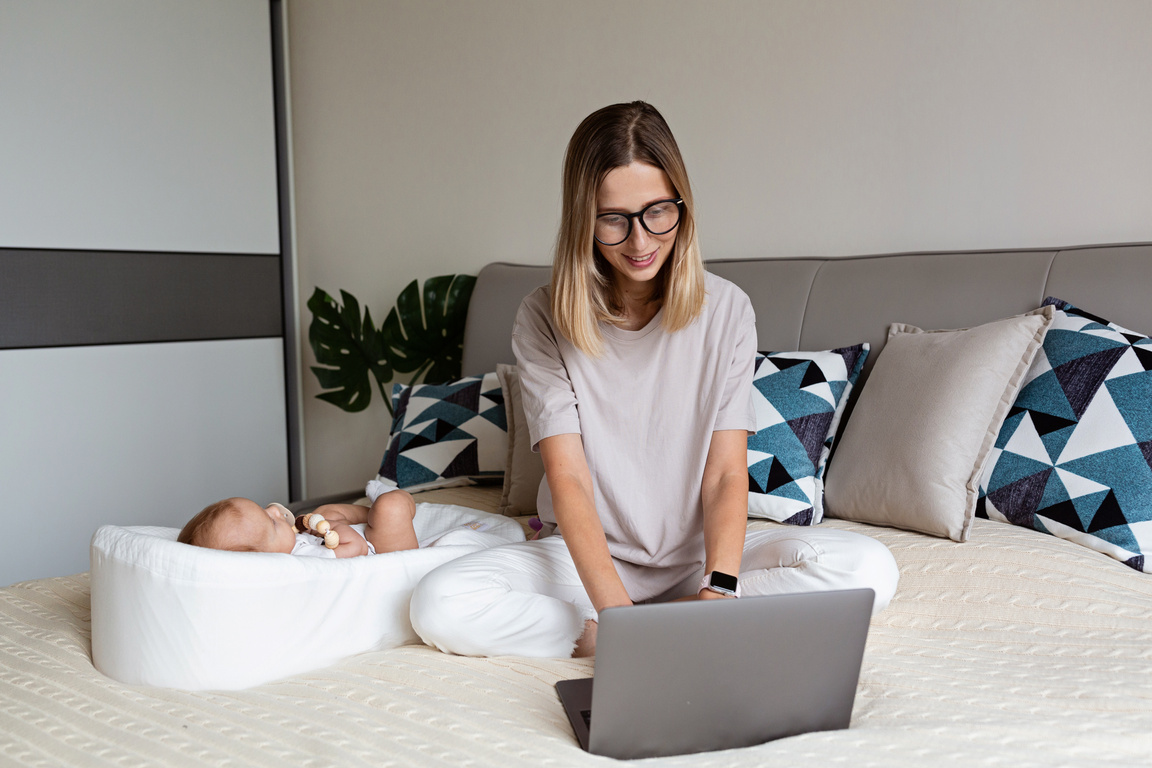 Mother Working on Laptop with Baby on the Bed